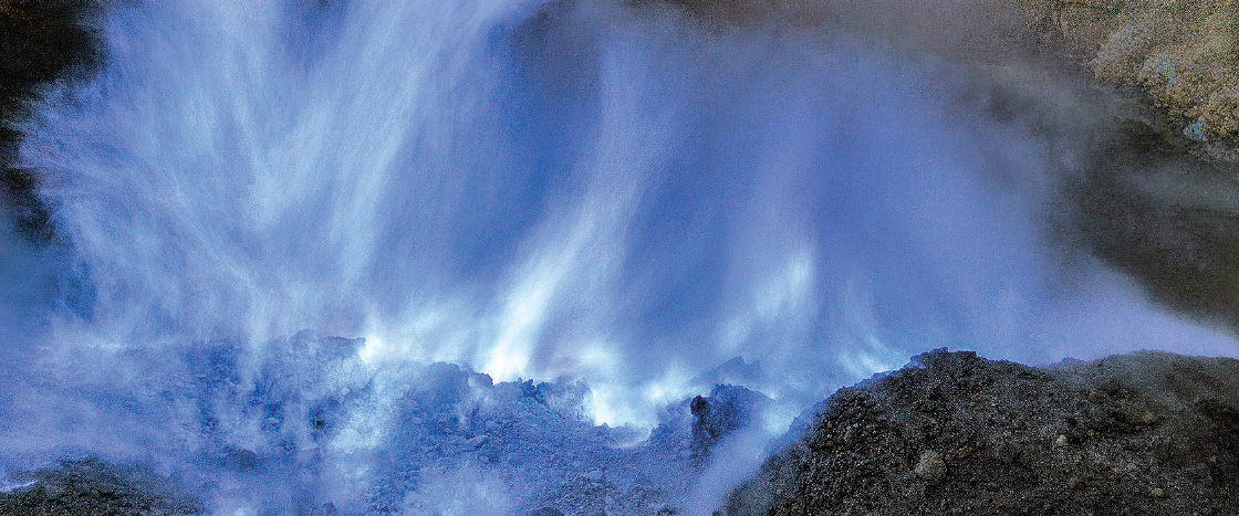 Blue flames and sulfuric gas rise from rocky volcanic vents at night